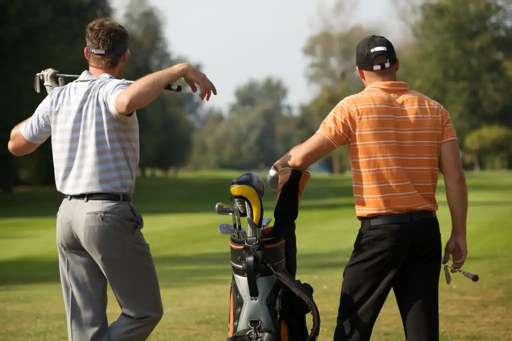 Two men face away from the camera to survey the green before them.
